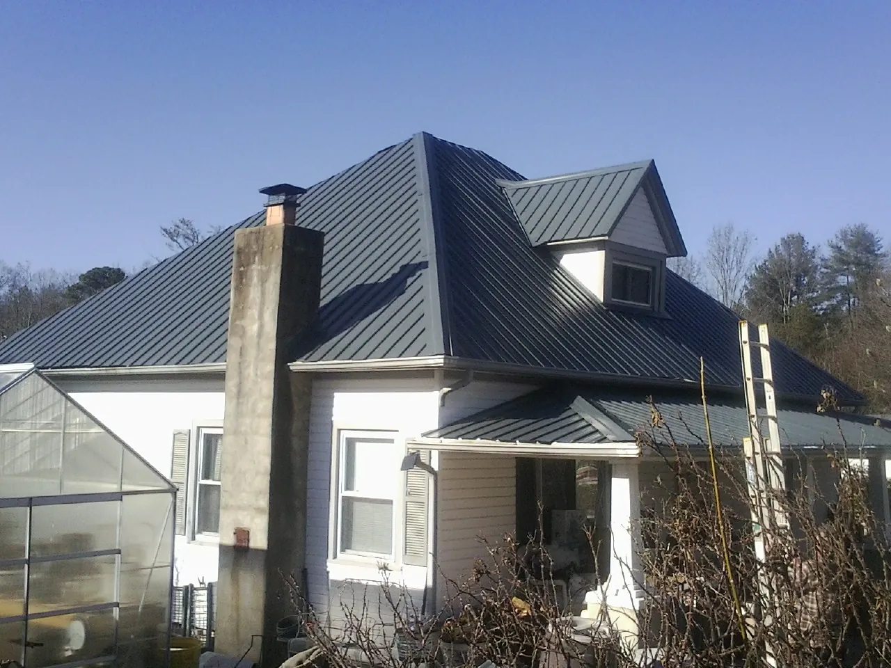 Dark blue standing seam metal roof on a white farmhouse with dormer — Slate & Tile Roof Repair by Roofing Brothers in Butte City