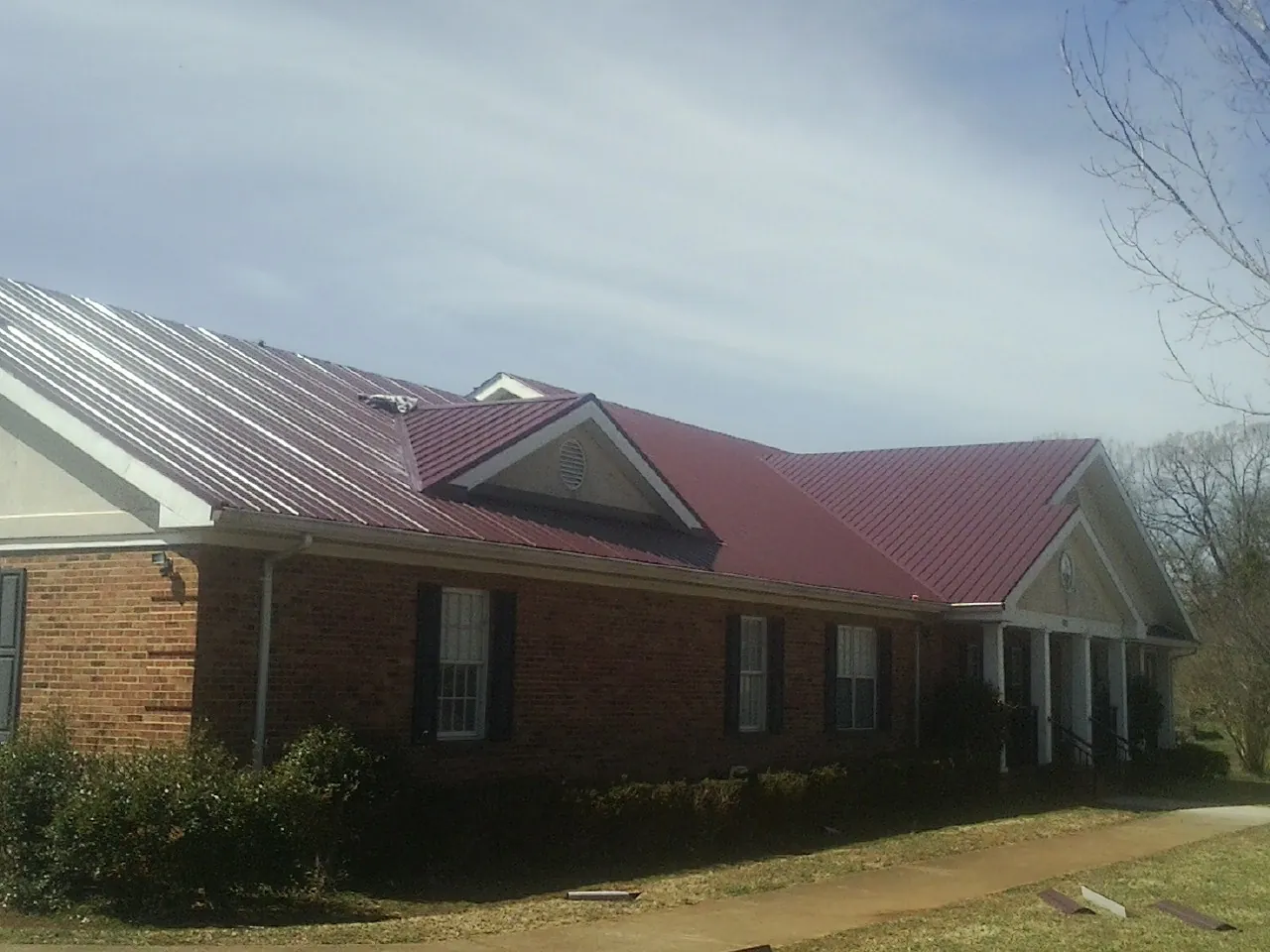 Red metal roof with gabled entries on a long brick building, from a Hail Damage Roof Repair job in Butte City