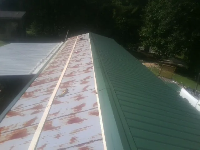 Old rusted panels beside newly installed green metal roofing — Wind Damage Roof Repair by Roofing Brothers in Butte City