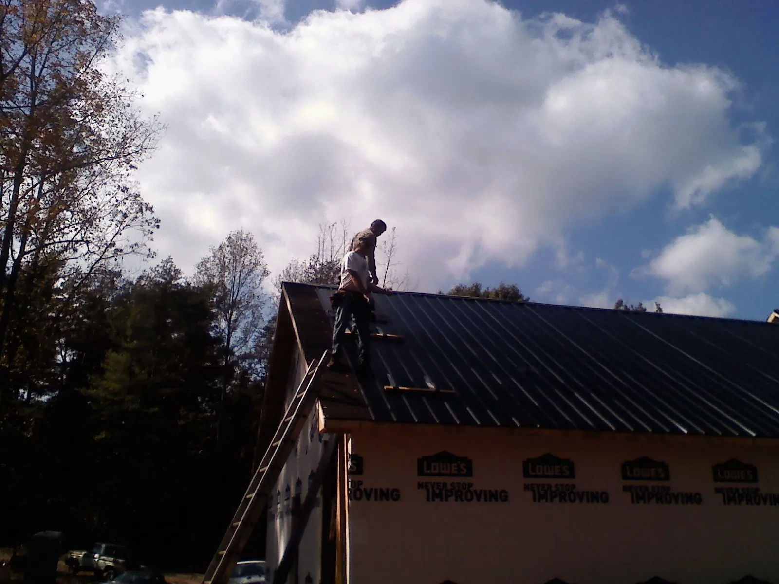 Roofer fastening dark metal panels high against a cloudy sky, from a Roof Inspection job in Butte City