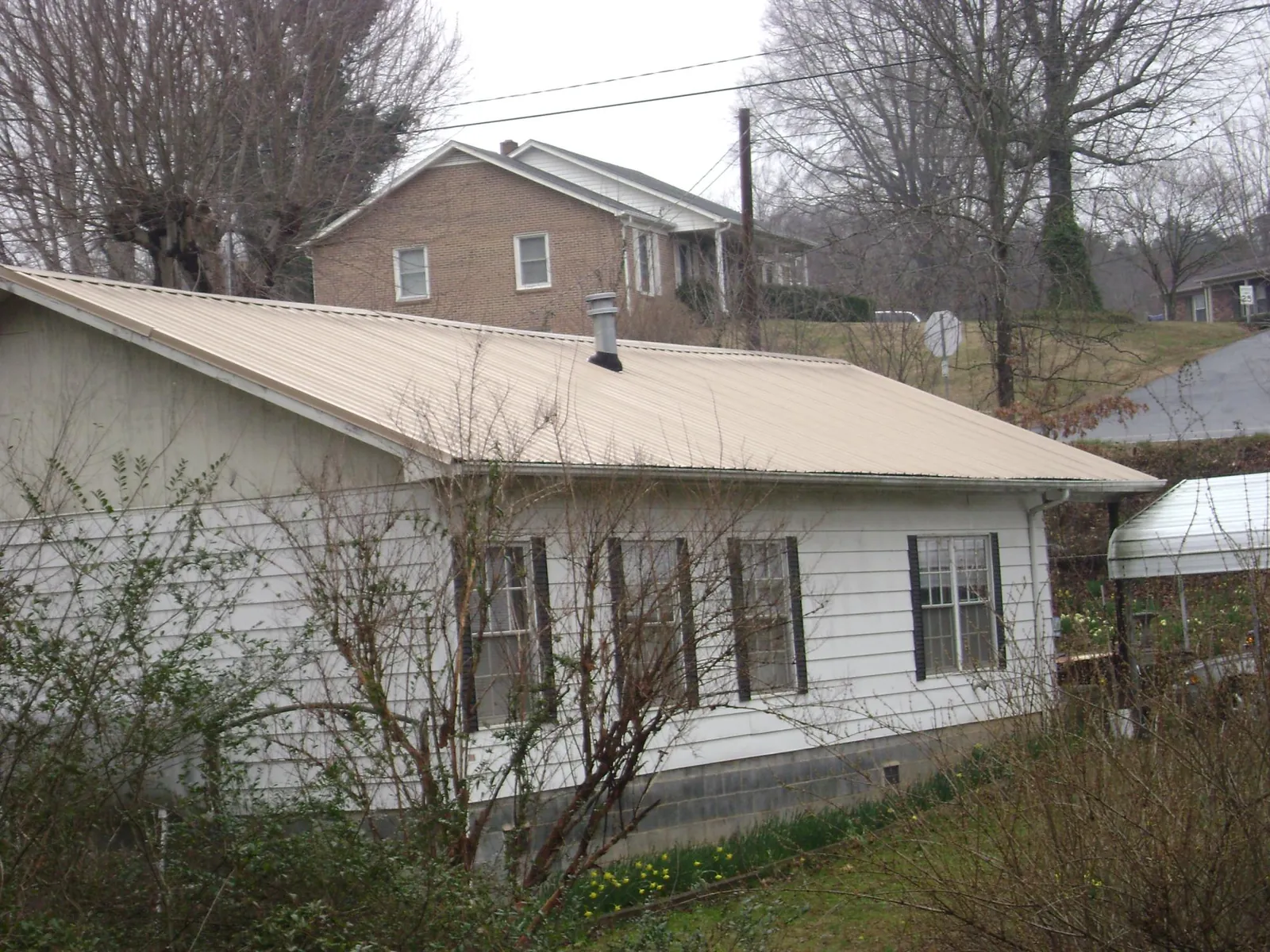Tan metal roof on a white sided house set into a hillside — Commercial Roofing by Roofing Brothers in Butte City